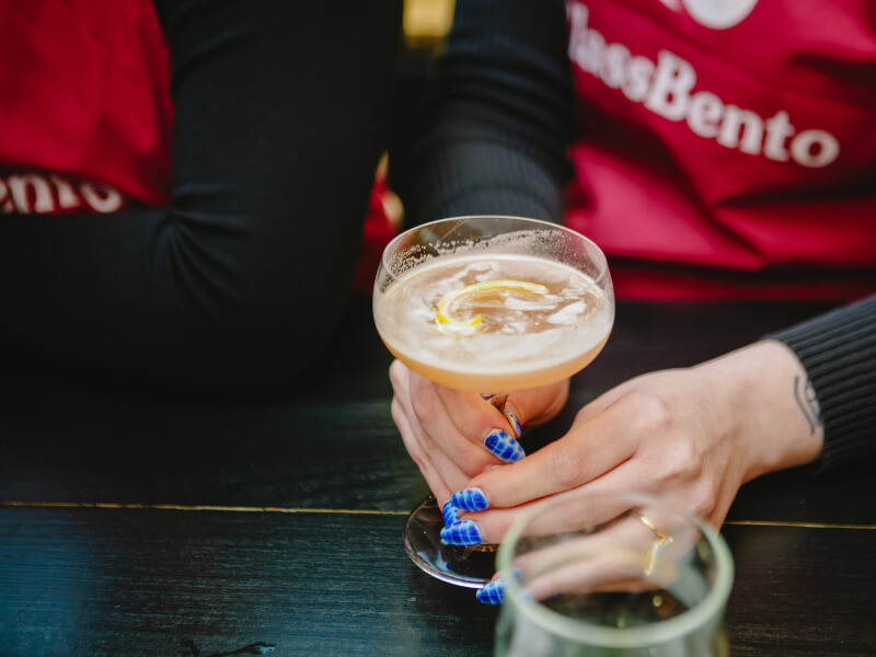 Close up of a person making a pale coloured cocktail in a glass